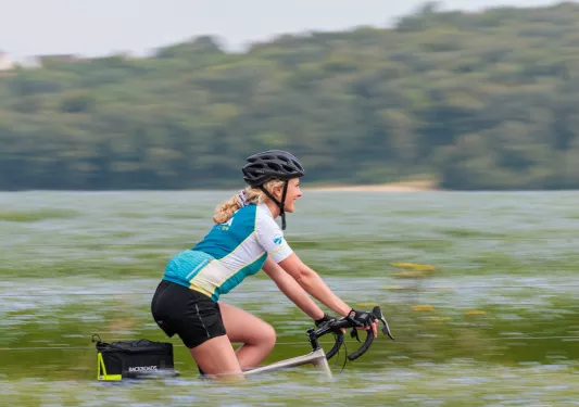 Woman riding a bike on a road, surrounded by crops and vineyards