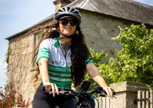 Woman smiling, while riding a bike with a stone building in the background