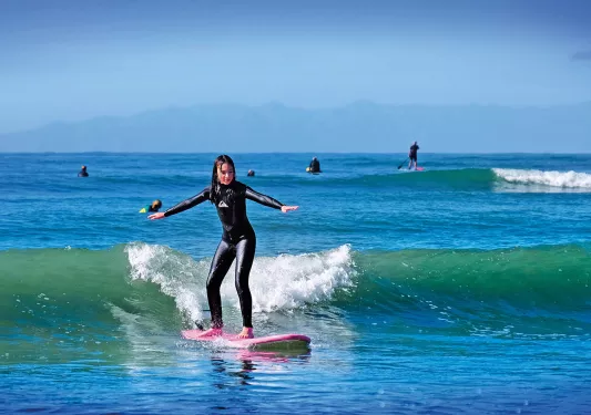Girl standing on a pink surfboard in the ocean