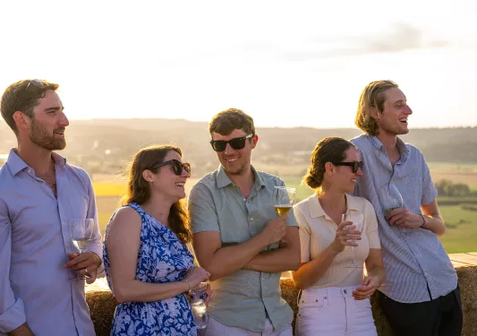Group of men and woman holding glasses of wine, with a valley in the distance