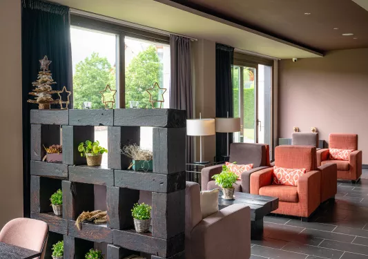 Indoor hotel reception area with cushioned chairs and plants scattered around the room