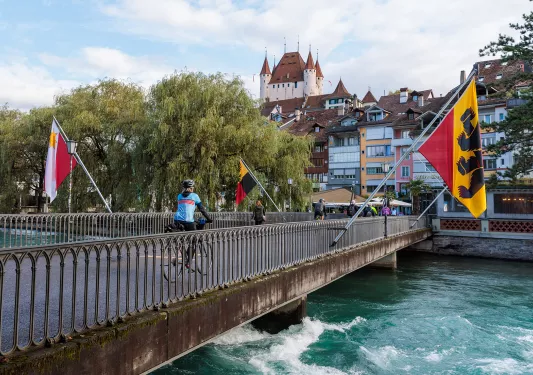 Woman biking across a bridge surrounded by large flags