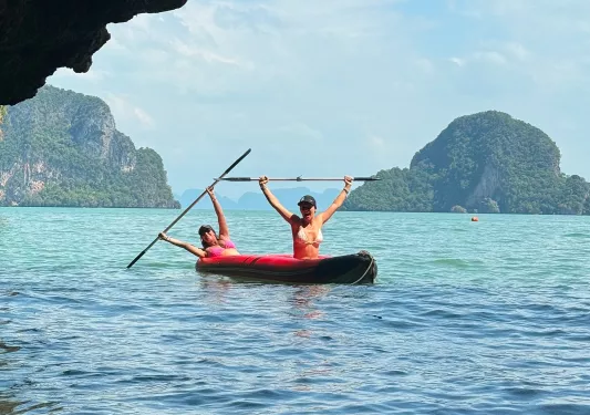 Two women on a red kayak, holding their paddles in the air