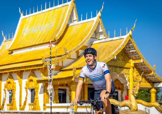 Man smiling while biking in front of a white and gold temple