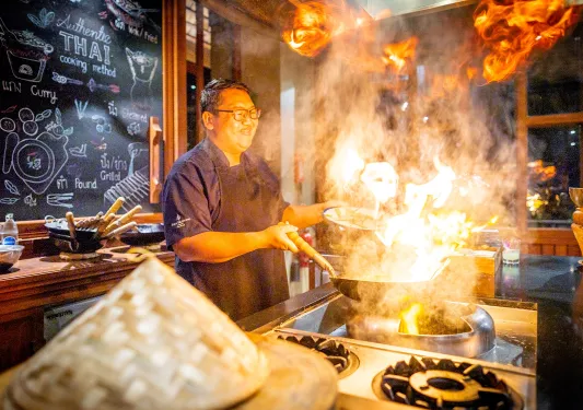 Man wearing an apron, cooking with a large wok creating large flames