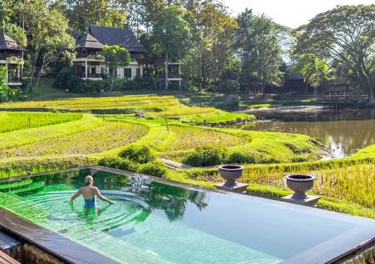 Woman standing inside of an outdoor pool, with large grass fields in the back