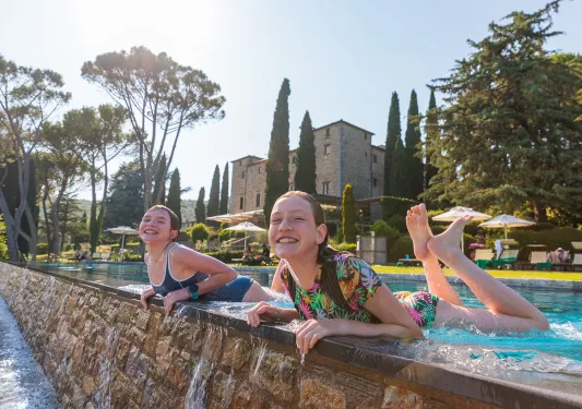Two girls smiling while leaning on the ledge of a pool