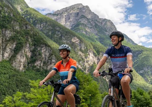 Two women smiling while riding bikes with tall mountains in the background