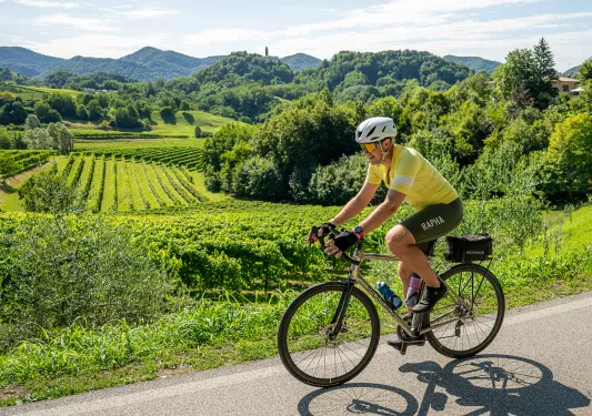 Man wearing yellow and green biking gear, riding a bike with crop fields in the background