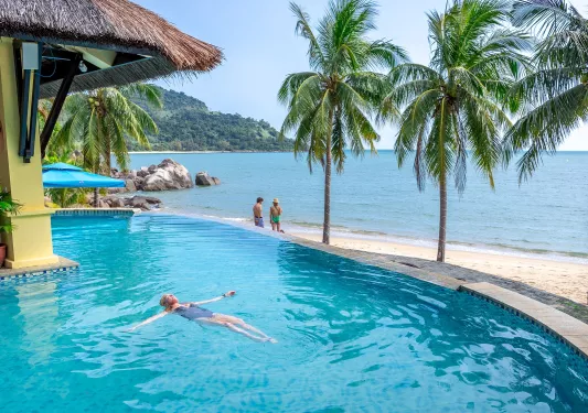 Woman floating in a pool, with views of the beach nearby