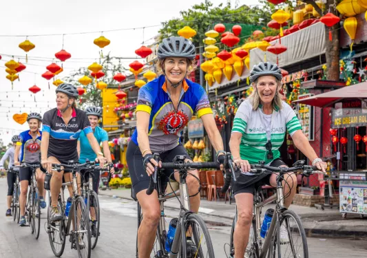Group of women riding bikes on a road with markets to the right