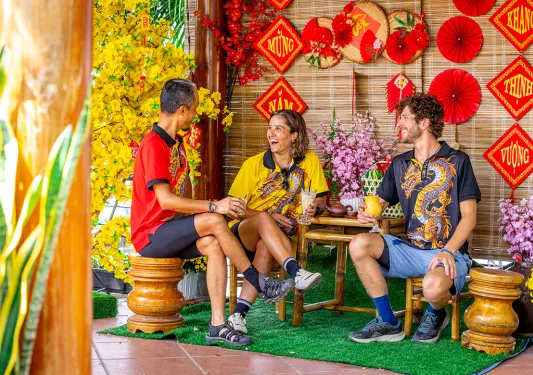 Two men and one woman sitting on wooden chairs in front of Vietnamese art pieces