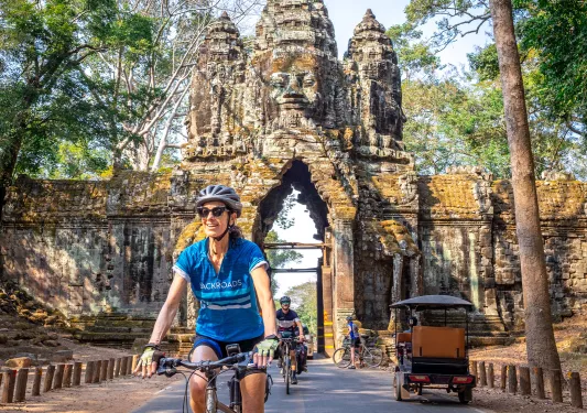 Woman smiling while riding a bike with a stone temple entrance in the background
