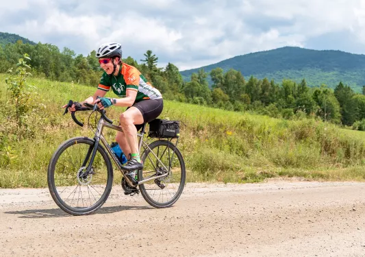 Woman riding a bike on a dirt road, with a grassy hill in the background