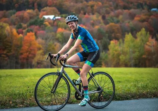 Woman smiling while riding her bike on an empty road, with a forest in the background