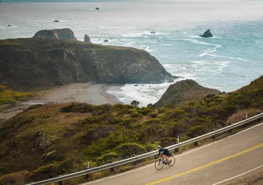 Person riding a bike on an empty road, with views of the ocean in  the distance