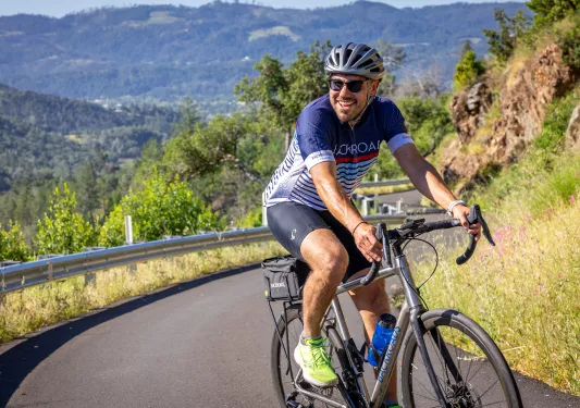 Man wearing biking gear and sunglasses, riding a bike on a hairpin road