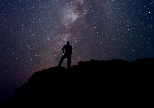 Silhouette of person standing on a cliff with the night sky in the background