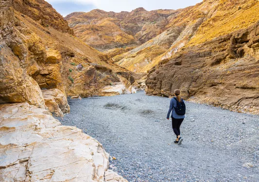 Woman walking a rocky trail in between two orange canyons