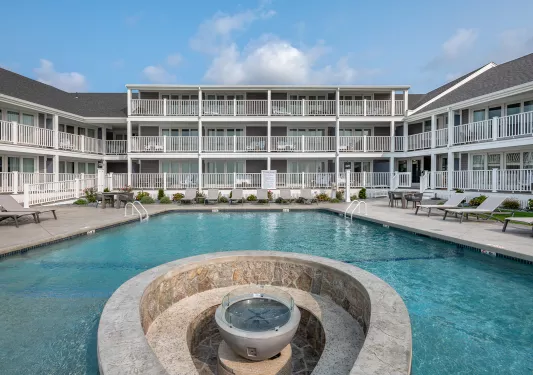 Outdoor pool with a fountain in the center and hotel building in the back