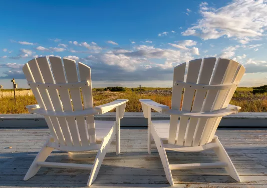 Two white chairs on an outdoor patio, looking out to a large valley