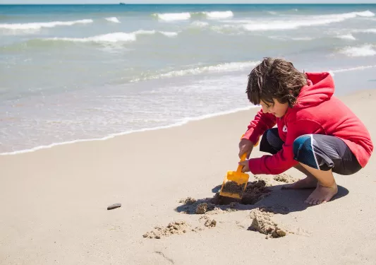 Boy on the beach, playing with the sand and a scooper