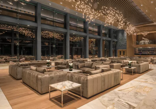 Large seating area with large windows and beige sofas, with hanging light fixtures