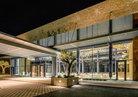 Exterior view of stone hotel building with large windows and trimmed trees in front