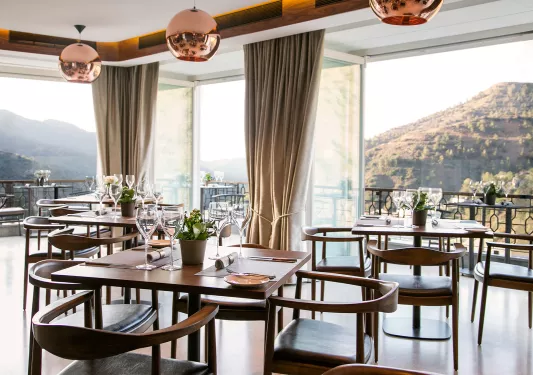 Restaurant with wooden dining tables and chairs, with large open doors in the background