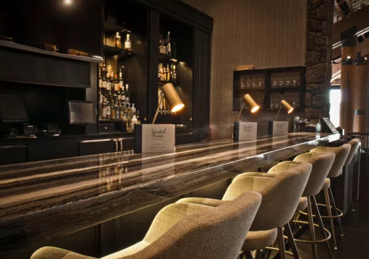 Dimly lit bar with cushioned stools and alcohol on the shelves in the back