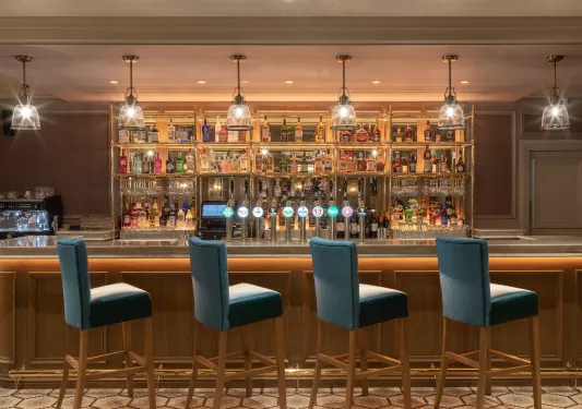 Bar counter with blue, cushioned chairs with alcohol along the shelves on the walls