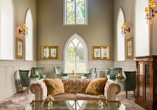 Lounge with cushioned green and red sofas and large, stained glass windows in the background