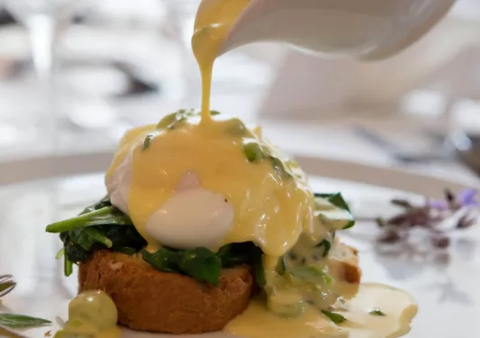Plate of eggs benedict, while pouring sauce over