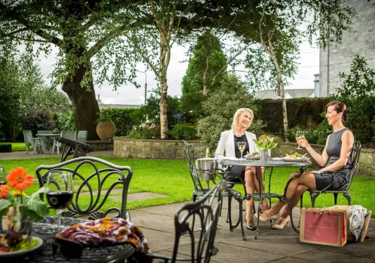Two women sitting outdoors in a garden, holding up glasses of wine