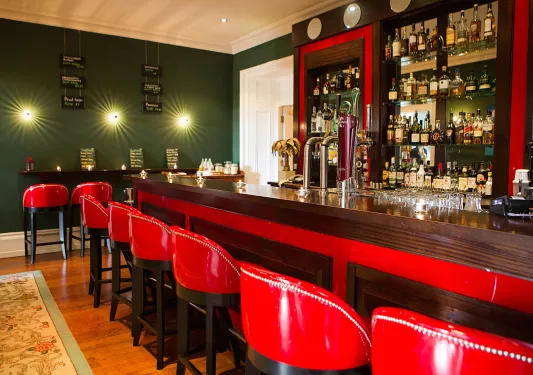 Bar and lounge with a wooden counter and red, leather stools