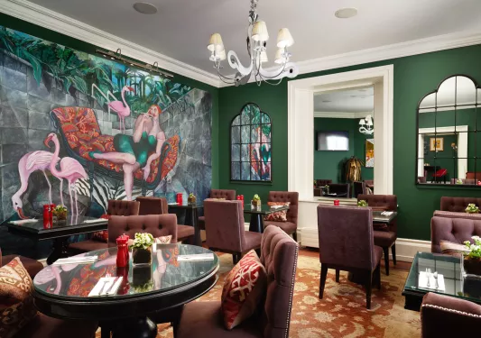 Dining hall with circular tables with cushioned chairs and large murals on the walls