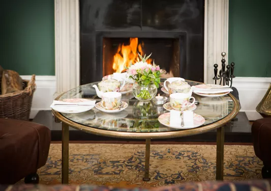Coffee table with teacups and coasters on top, in front of a fireplace