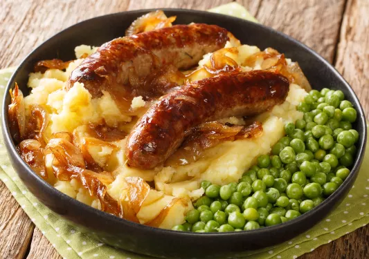 Bowl of bangers and mash with a side of peas