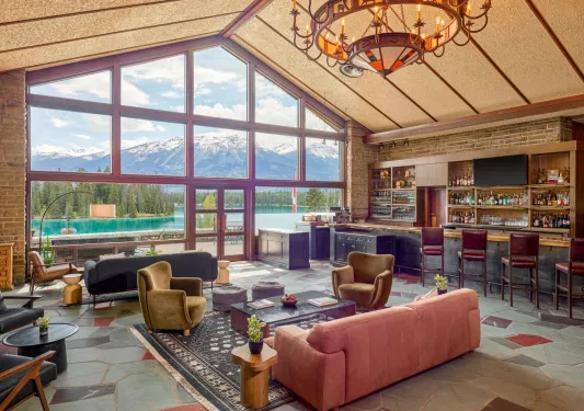 Bar and lounge with cushioned sofas and a bar counter to the right, with large windows looking out to a lake