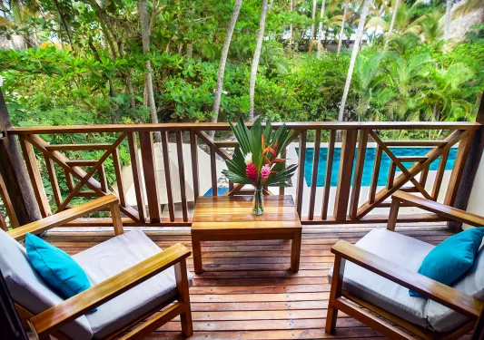 Wooden balcony with two cushioned chairs and a small table with a flower on top
