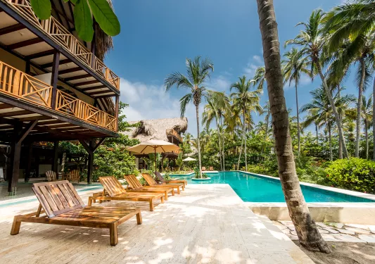 Outdoor pool surrounded by reclining, wooden chairs, with palm trees to the right