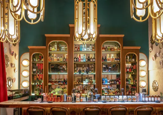 Bar with alcohol bottles on the wall and a counter full of glasses and small light fixtures