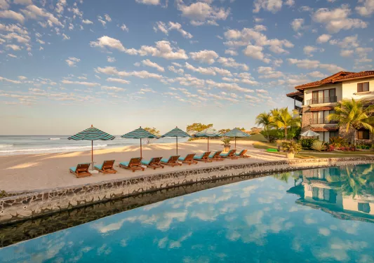 Outdoor pool with a row of reclining chairs looking out to the beach