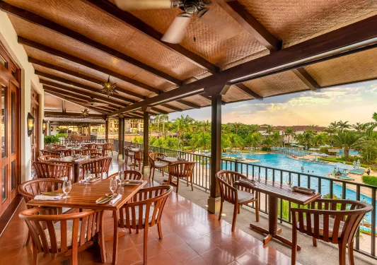 Outdoor tiled patio with wooden chairs and tables, with view of an outdoor pool in front