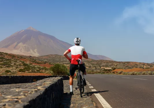 Man in a white and red shirt, riding a bike on a road with mountains in the distance