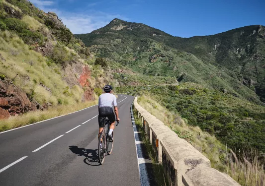 Person riding their bike on a road with large, grassy mountains in the distance
