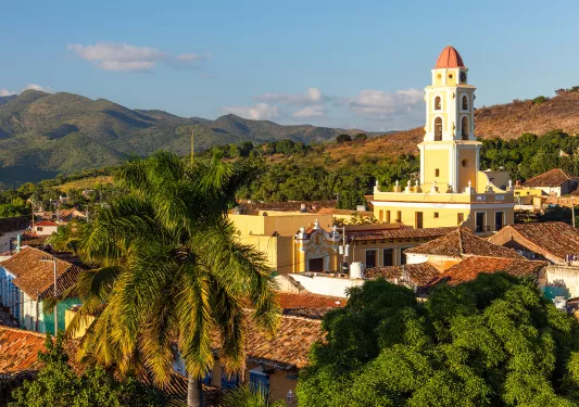 Sky view of a yellow church in the distance, surrounded by trees