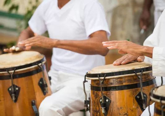 Two men wearing white, playing bongos
