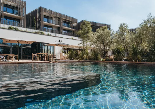 Outdoor pool surrounded by trees, with a hotel building in the background