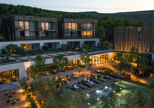 Exterior, evening view of a large hotel complex with an outdoor pool surrounded by trees